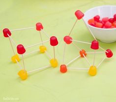 several pops are placed next to a bowl of gummy bears on a green surface