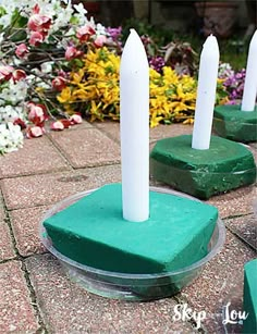 four candles sitting on top of green bases in front of flowers and bushes with white stems sticking out of them