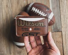 a person holding up a wallet with footballs in the background