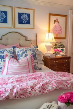 a bed with pink and blue pillows in a bedroom next to a lamp on a dresser