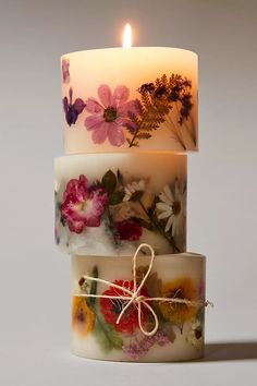 three stacked candles with flowers on them and one candle lit in the middle, both decorated with twine string