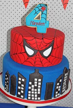 a spiderman birthday cake with the number four on it's face and city skyline