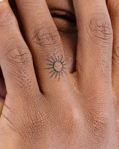 a person's hand with a small sun tattoo on the middle finger and fingers