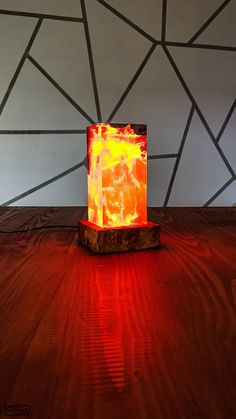 an orange light sitting on top of a wooden table next to a wall with geometric designs