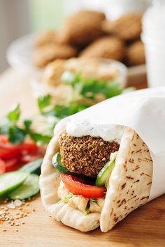 a pita sandwich with vegetables and sauce on it sitting on a cutting board next to other food items