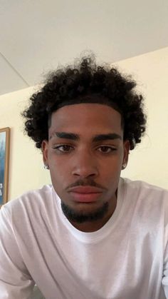 a young man with curly hair is looking at the camera while wearing a white t - shirt