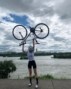 a person holding up a bike over their head near the water and clouds in the sky