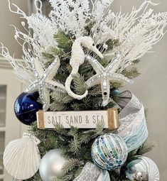 a white christmas tree with ornaments and a sign that says salt, sand & sea