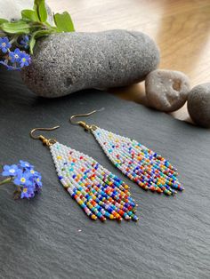 two pairs of beaded earrings sitting on top of a table next to rocks and flowers