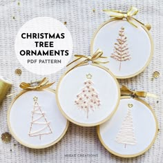 four christmas tree ornaments with gold ribbon and bows on white fabric next to twine spools