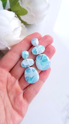 a person is holding three blue and white earrings in their hand next to some flowers