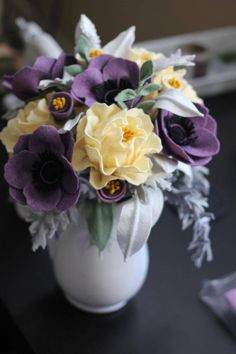 a white vase filled with purple and yellow flowers