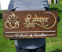 a person holding up a wooden sign in front of some green grass and trees with the words india anishka written on it