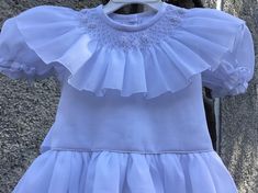 White smocked dress. Fully lined and ties on the back. Will be an appropriate dress for a flower girl, Christening or confirmation. Two are available SIZE 2T SIZE 6T For custom orders allow 2-3 weeks for delivery. Elegant Summer First Communion Dress, Elegant Baptism Dress With Smocked Back, Elegant Smocked Ruffle Dress For Baptism, Elegant Dress With Smocked Back For Baptism, Elegant Smocked Dresses For Baptism, Elegant Baptism Dress With Smocked Bodice, Elegant Fitted Baptism Dress With Smocked Bodice, Elegant White Smocked Dress For Baptism, White Baptism Dress With Ruffles And Fitted Bodice