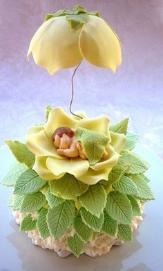 a small yellow flower with green leaves on it's head is sitting on a white surface