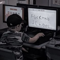 a young boy sitting in front of two computer monitors with writing on the monitor screen