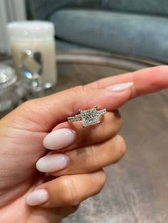 a woman's hand holding a diamond ring on top of her finger, in front of a glass table