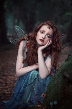 a woman with red hair is sitting in the woods