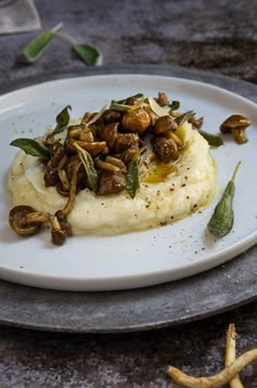 a white plate topped with mashed potatoes covered in nuts and sage leaves on top of a table