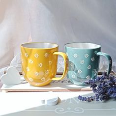 two coffee mugs sitting next to each other on top of a wooden tray with flowers