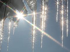 the sun shines brightly through icicles hanging from a tree in front of a blue sky