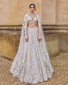 This lehenga set features three-dimensional embroidery in a bold floral pattern in thread, pearl, sequin and beads. The blouse has a plunging neckline and shows exaggerated pearl tassels. It is paired with a matching four sided embroidered dupatta. It is paired with an optional embroidered organza cape with a trail at the back.From Seema Gujral's A Royal Affair collection. DELIVERY TIMEPlease allow 8-12 weeks for your outfit to arrive. FABRIC DETAILSNet Professional cleaning only. Seema Gujral Lehenga, Glamorous White Hand Embellished Sets, Glamorous White Choli With Pearl Embroidery, White Glamorous Sets With Resham Embroidery, Glamorous White Sets With Resham Embroidery, Glamorous White Choli With Traditional Drape, Glamorous White Choli For Reception, Glamorous White Festive Lehenga, Glamorous White Embellished Choli