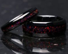 two black wedding bands with red and blue glitter inlays, on a reflective surface