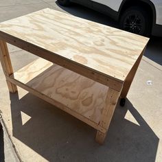 a table made out of plywood sitting on the sidewalk next to a parked car