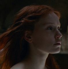 a woman with red hair is staring into the distance