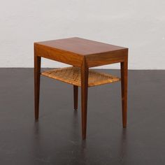 a small wooden table sitting on top of a black floor next to a white wall