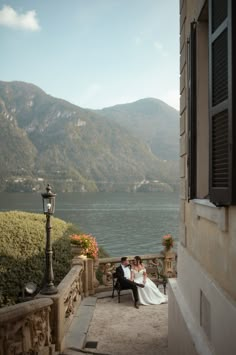 a bride and groom sitting on a balcony overlooking the lake with mountains in the background