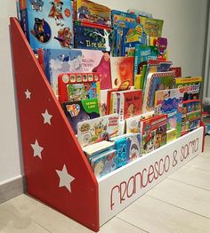 a red and white book stand filled with children's books on top of a wooden floor