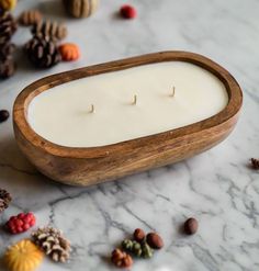 two candles in a wooden holder surrounded by nuts and pine cones on a marble surface