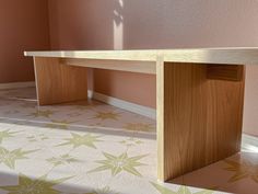 a wooden table sitting on top of a floor next to a pink wall with flowers