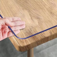 a person's hand is holding the edge of a wooden table with blue tape on it