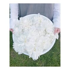 a person holding a plate with white flowers in it on the grass and their hands