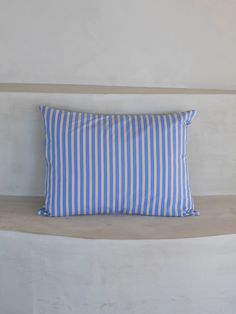 a blue and white striped pillow sitting on top of a cement bench next to a wall