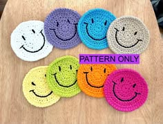 six crocheted smiley face coasters on a wooden table with the faces painted in different colors