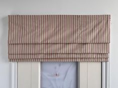 an open window with a striped roman blind on the top and bottom half, in front of a white wall