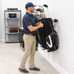 a man standing next to a wall with golf bags and clubs hanging on the wall