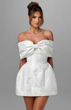 a woman wearing a short white dress with a big bow at the waist and neckline