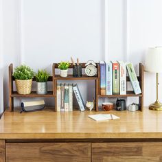 a wooden desk topped with lots of books and office supplies next to a lamp on top of a dresser