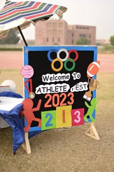 a welcome sign for athletes is displayed in front of a beach chair and table with an umbrella