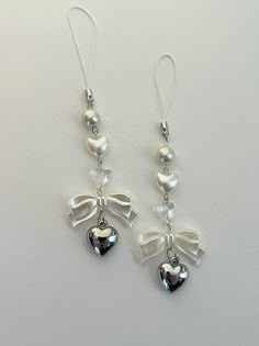 two silver bells with bows and pearls hanging from the earwires on a white background