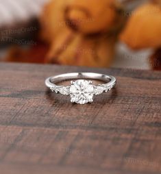 a white gold engagement ring with three stones on it sitting on top of a wooden table