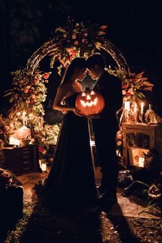 a bride and groom pose with their pumpkins in front of an arch decorated with candles