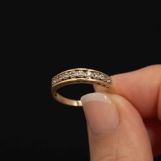 a hand holding a gold ring with three diamonds on the top and bottom side, in front of a black background