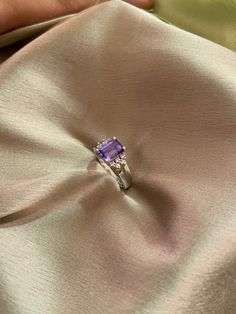 a woman's hand holding an engagement ring on top of a satin material cloth