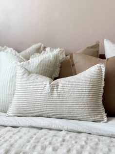 a bed topped with lots of pillows next to a white headboard and pillow case