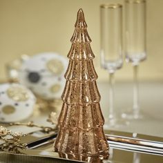 a glass christmas tree sitting on top of a table next to wine glasses and silverware